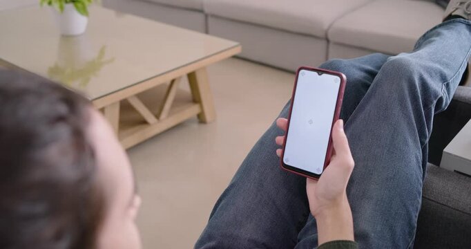 African American man lying on grey sofa holding red phone with loading icon, waiting on load