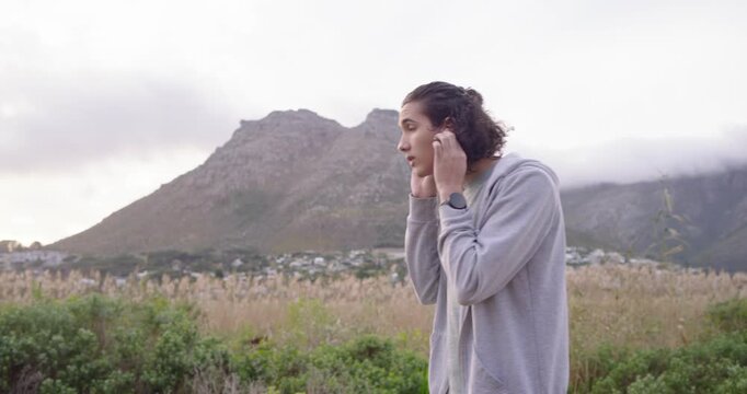 Man checking smartwatch fitting earbuds to listen in hoodie walking past mountain, copy space