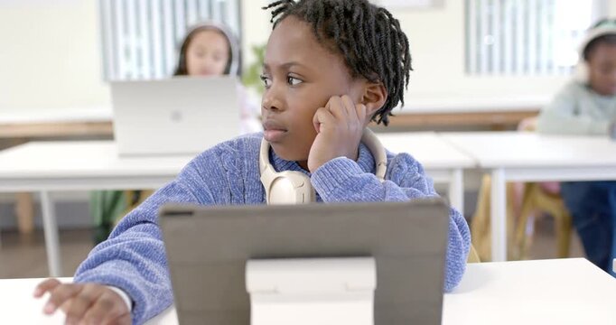 African American youth student glancing left, swiping tablet on white stand, studying in classroom