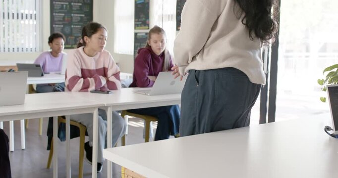 Female teacher standing, turning, gesturing after perching, teaching code with laptops, copy space