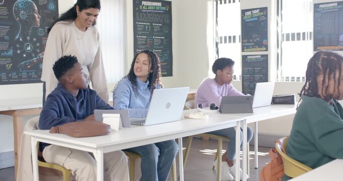 Teenage African American students and Indian teacher entering lab, leaning over laptop guiding code