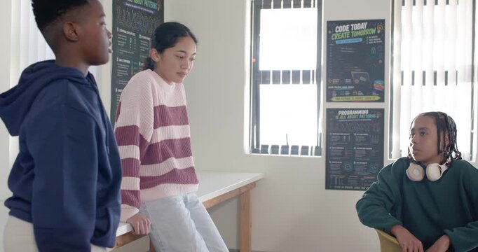 Diverse youths discussing project in coding lab, left student speaking, female gesturing on counter