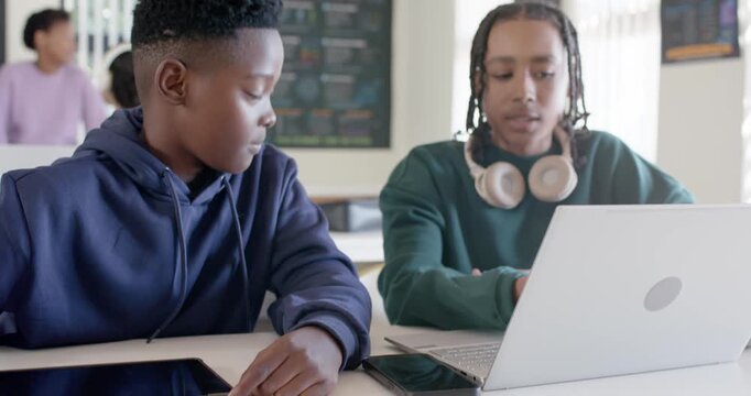 African American teen male students reaching tablet, working while right student typing on laptop
