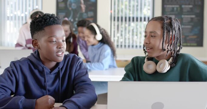 African American male teens talking, left teen starting chat, reviewing laptop and headset in class