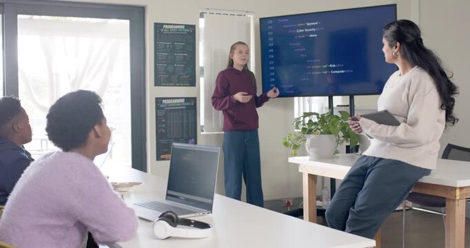 Teen African female starting presentation, pointing to code on monitor in lab, teaching peers