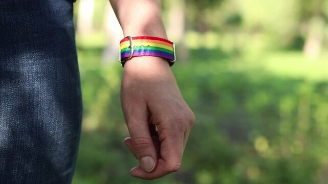 Close-up of a person's hand with a rainbow bracelet on a nature background. A woman's hand with a fabric strap in rainbow colors (LGBT symbolism) on her wrist. A symbol of pride and equality