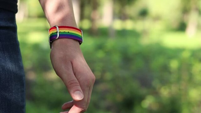 Close-up of a person's hand with a rainbow bracelet on a nature background. A woman's hand with a fabric strap in rainbow colors (LGBT symbolism) on her wrist. A symbol of pride and equality