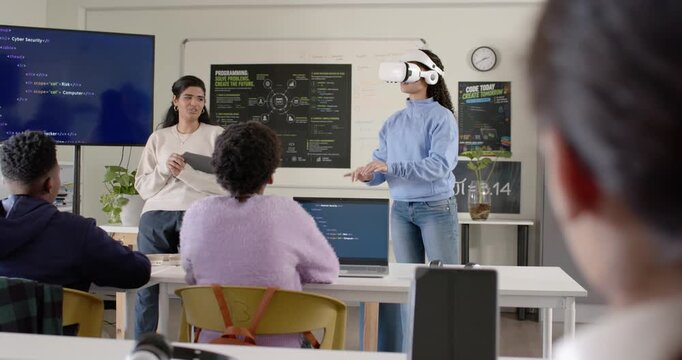 Diverse peers watching presenter cueing VR user putting on white headset, gesturing at code in lab