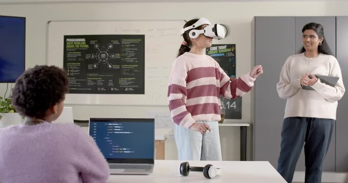 Diverse females, Indian mentor watching student putting on white headset and gesturing to test code