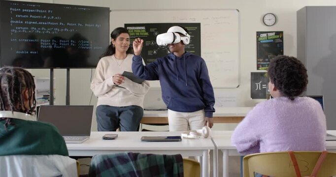 Instructor nodding, class watching teen with VR headset reaching and pinching for demo, tablet