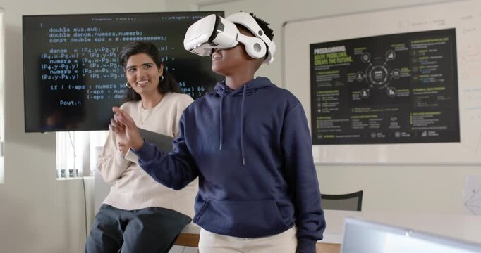 Diverse pair Indian woman tapping tablet, African American teen in VR headset gesturing in lab demo