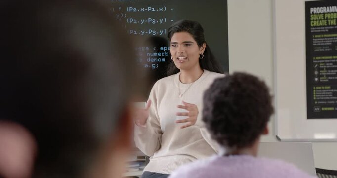 Indian woman sitting in class in cream sweater starting clasping hands explaining code on display