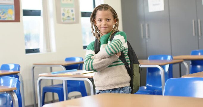 African American boy shifting, crossing arms, posing with pack in front of class as camera zooming