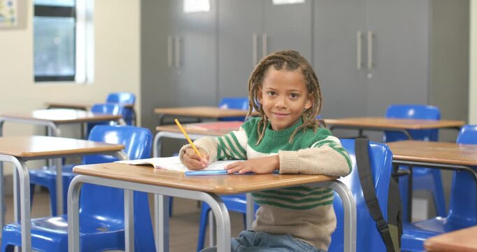 African American schoolboy writing with pencil at desk in class, responding to workbook and smiling