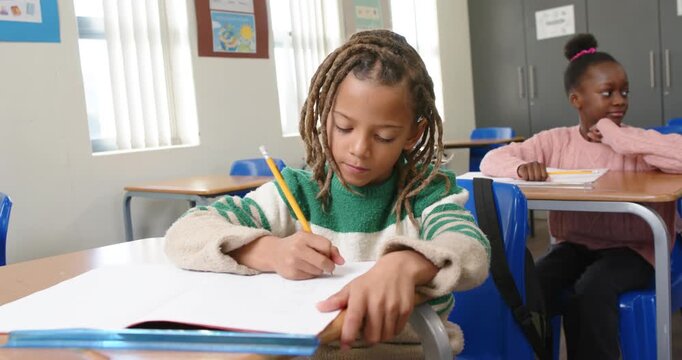 African American girls at school child in green top writing work in notebook with pencil, pausing
