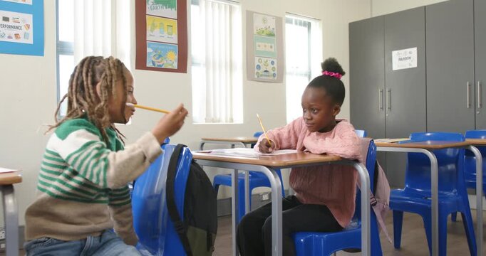Children at school after shifting boy kneeling with pencil near girl writing, seeking attention