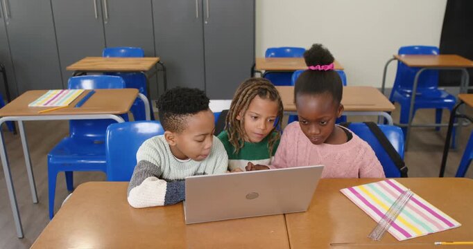 Diverse school-aged students leaning toward open laptop, typing and using touchpad for assignment