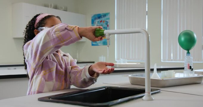 African American teen at lab checking green balloon bottle opening tap handwashing before returning