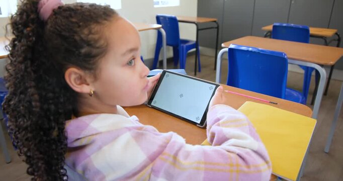 Teenage girl sitting at desk holding tablet adjusting grip keeping screen readable by yellow folder