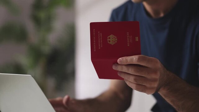 Young man holding German passport while booking railway tickets on laptop