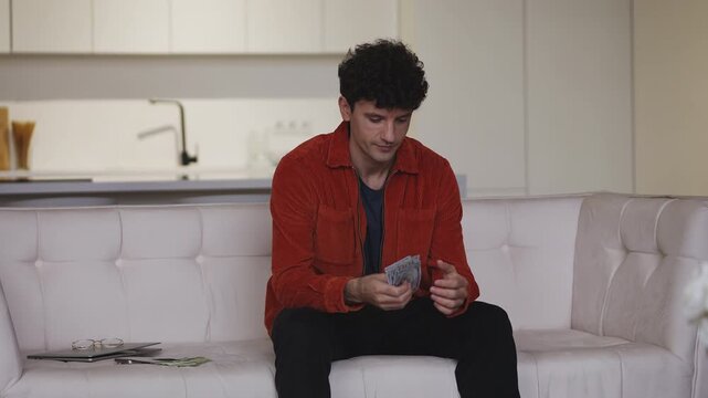 Successful young male entrepreneur counting money on couch, startup income