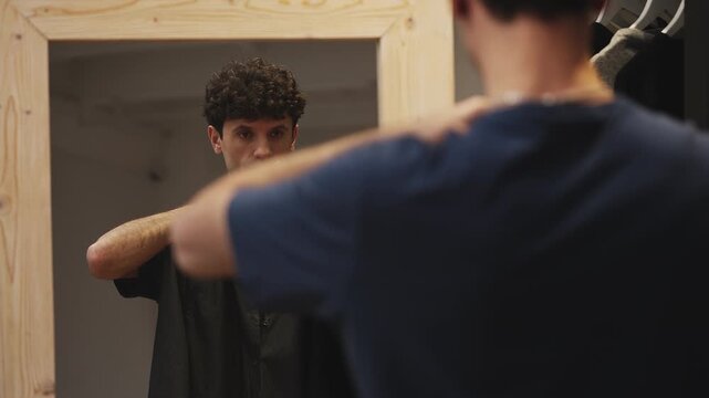 Young male choosing between jackets in front of mirror, getting ready for a date