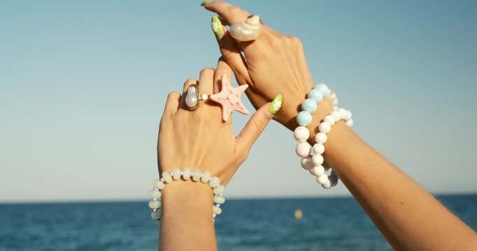 Woman's hands wearing shell jewelry dancing gently with a beautiful calm sea in the background