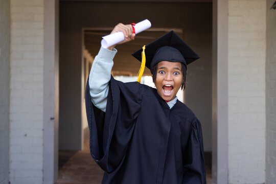 African youth cheering, holding rolled diploma red ribbon at entry, wearing gown cap yellow tassel