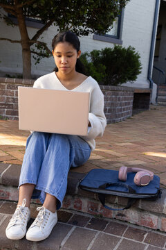 Child female sitting on brick step using laptop at porch with navy sleeve and pink headphones