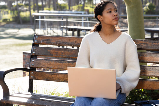 Asian girl child sitting on weathered wooden bench in park using rose-gold laptop, copy space