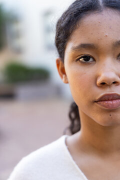 Child gazing at camera, showing skin detail, wearing plain light top and stud earring in courtyard
