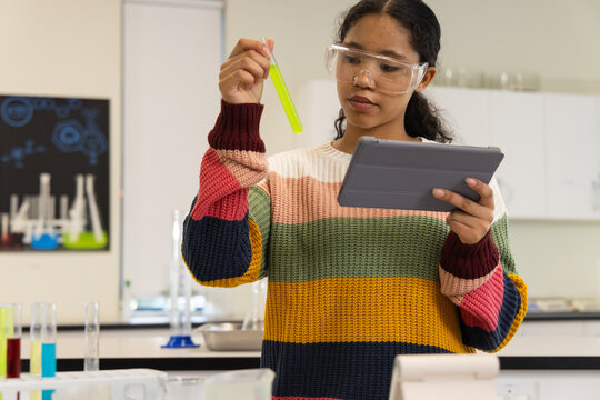 Child female student holding neon yellow-green test tube and noting on tablet in school lab