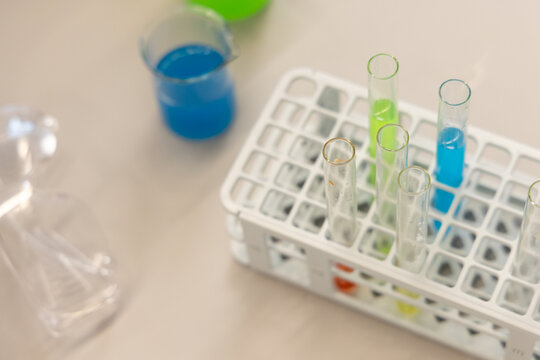 Test-tube rack holding glass tubes with blue and green liquids on beige countertop, blurred beaker
