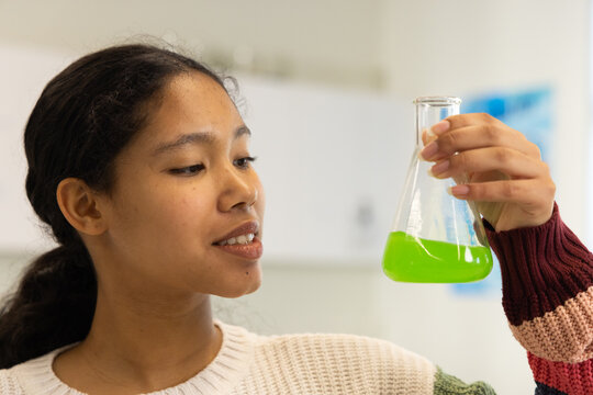 Child examining flask with neon green liquid in school lab wearing cream sweater with maroon stripe