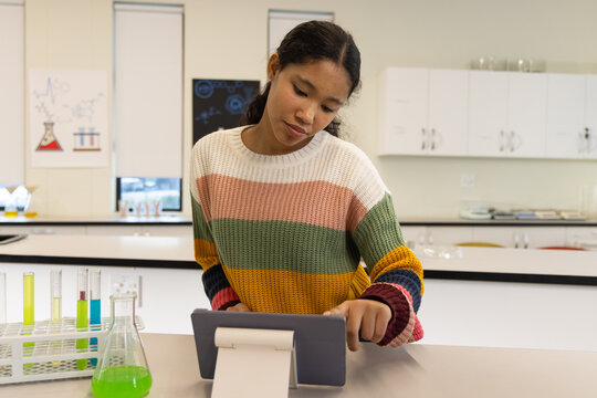 Female child in striped sweater using tablet on stand at lab with test tubes, green flask