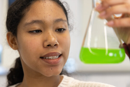 Female child gazing at conical Erlenmeyer flask held by hand in school lab wearing knit sweater