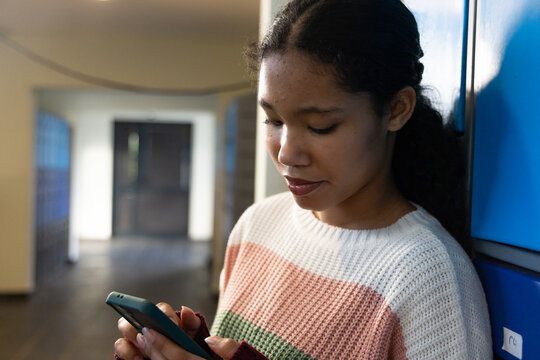 Female child leaning against row of blue lockers in school corridor, holding smartphone, copy space