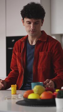Young man taking pill with water at home, daily vitamins for health support