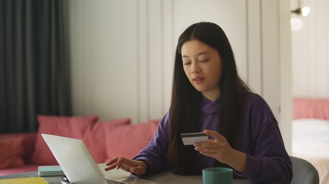 Happy Asian woman shopping online on laptop and entering credit card details
