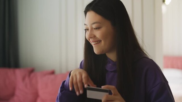 Smiling Korean woman entering credit card number on laptop while shopping online