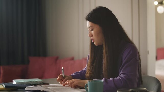 Young Korean woman studying at home, reading a book and taking notes
