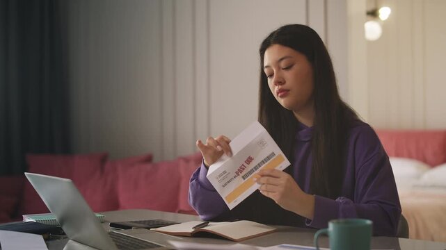 Young Korean woman reading overdue electricity bill, shocked by high cost