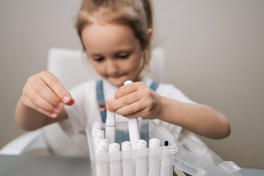 Little girl hands taking marker pens from clear storage box, getting ready for drawing activity, exploring creativity and learning through art at home.