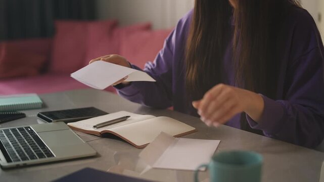 Young woman opening envelope and reading utility bill, checking daily mail