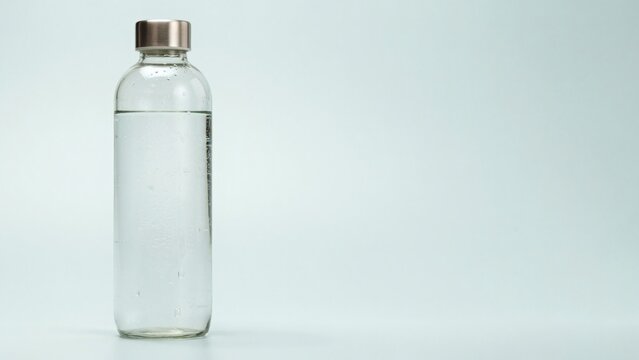 Clear glass water bottle with metal cap isolated on light blue background with topped minimalist metallic cap