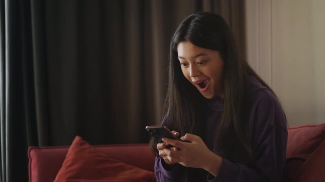 Young Asian woman receiving great news by text, celebrating business grant