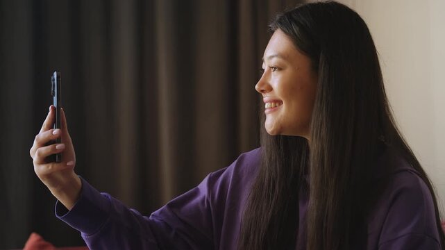 Smiling Asian woman answering video call, talking to relatives via mobile app