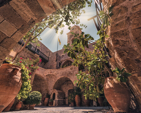 Sunlight enters the arcaded inner courtyard of fortified Toplou Monastery near Sitia in eastern Crete, framed by stone walls and large ceramic pots.