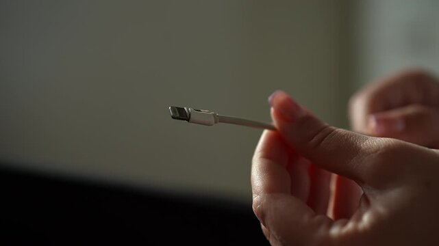 Hands holding and examining frayed damaged charging cable for mobile device. Concept of need for replacement and of planned obsolescence and electronic waste, close-up, slow motion.
