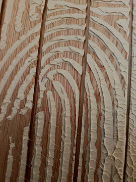 Textured wooden facade with decorative application of cream-colored plaster in wavy lines.